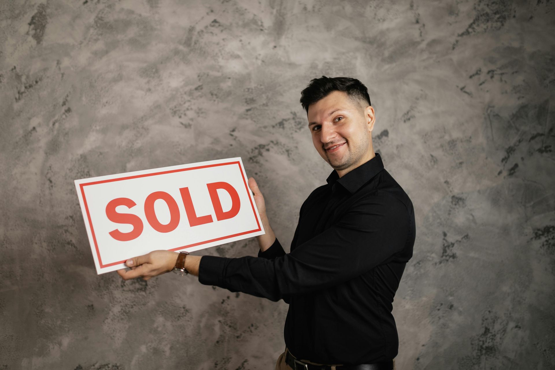 A man in a black shirt is holding a sold sign.