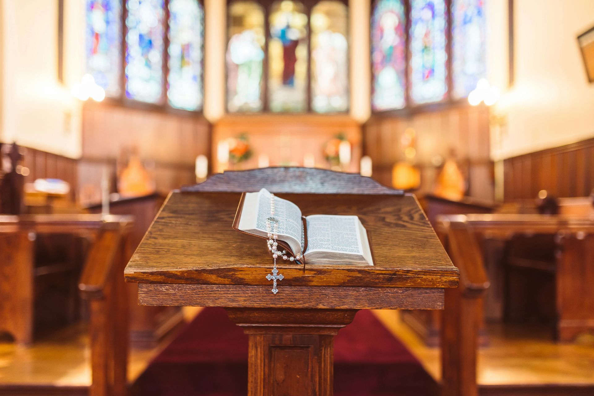 A bible and rosary are on a wooden podium in a church.