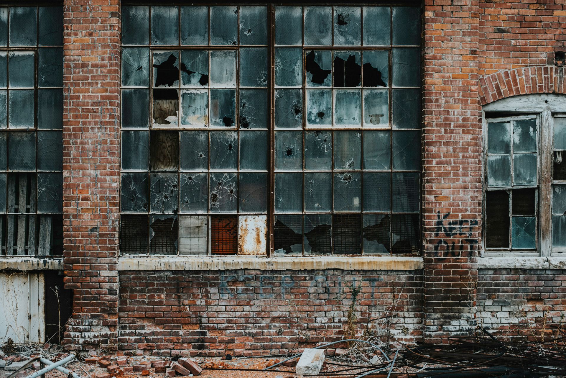 Dilapidated green wooden house with boarded-up windows and overgrown foliage.