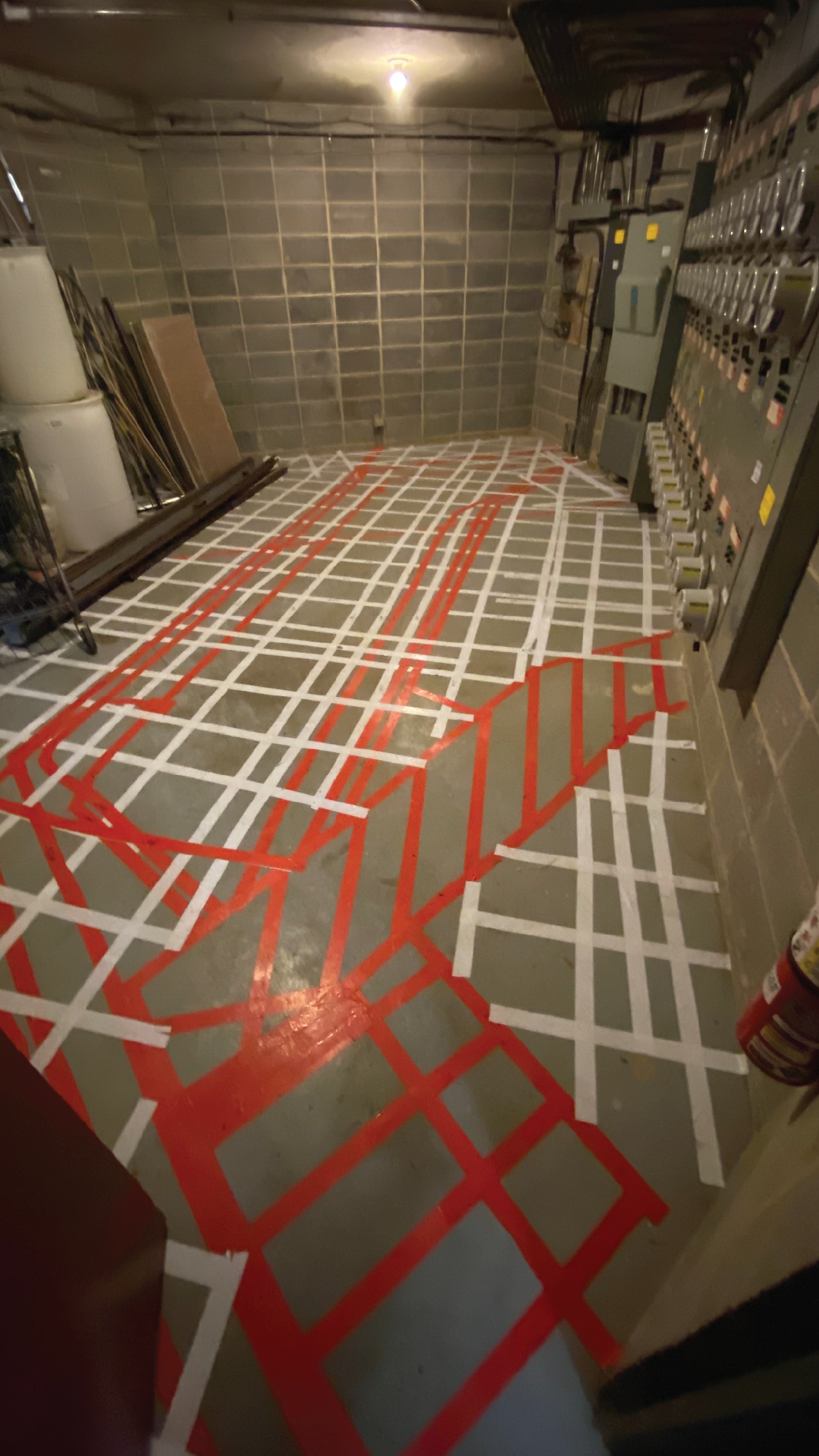 A room with a lot of red and white tape on the floor to show where the underground utilities are found.