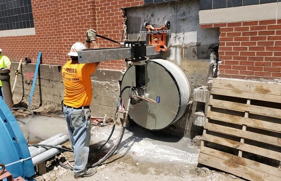 A professional from Cobra Concrete is using a core drilling machine to cut a hole in a brick wall.