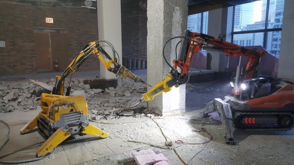 Two robots are breaking concrete in a building.
