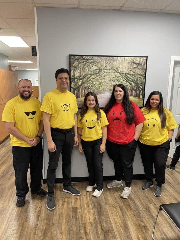 A group of people wearing yellow shirts with smiley faces on them are posing for a picture.