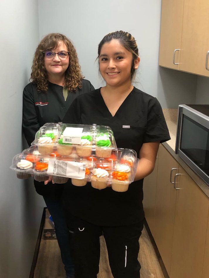 Two women are holding a tray of cupcakes in a kitchen.