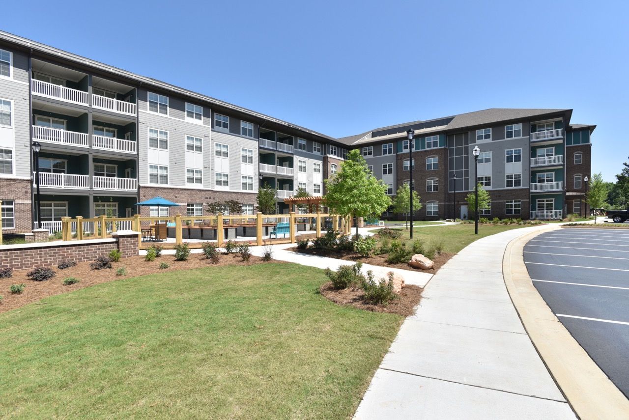 Exterior view of a modern apartment complex with balconies, landscaping, and a curved sidewalk.