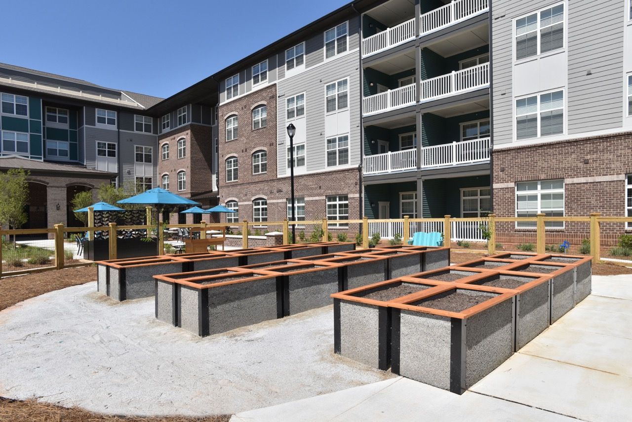 Outdoor communal courtyard with raised concrete planters and benches in front of a multi-story apartment building.