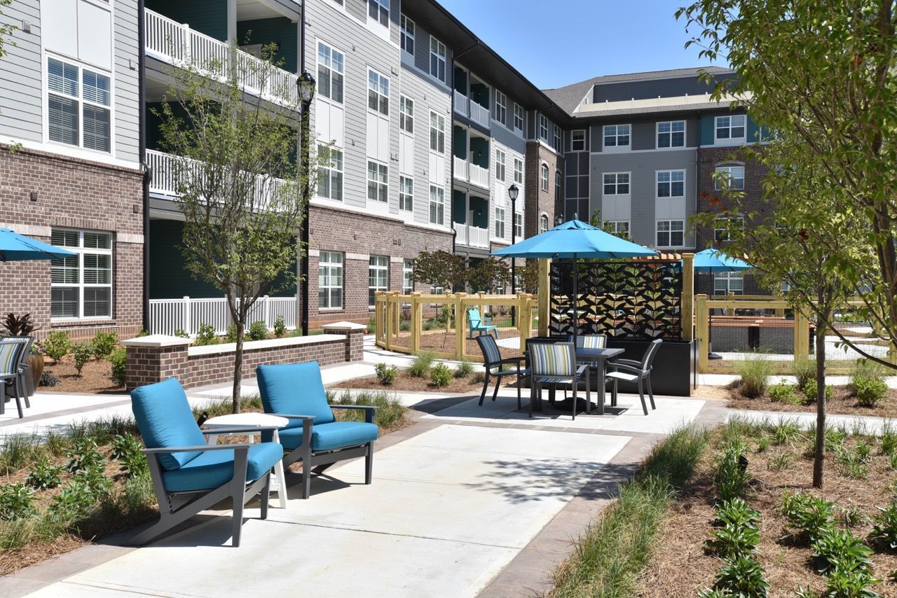 Outdoor community courtyard with blue cushioned chairs, tables, umbrellas, and landscaped paths.