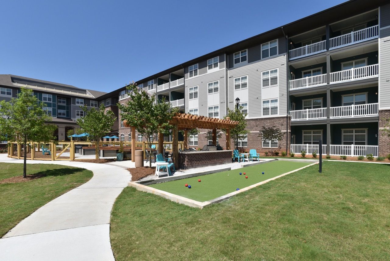 Exterior view of a modern apartment complex with a central courtyard, gazebo, and walking path.