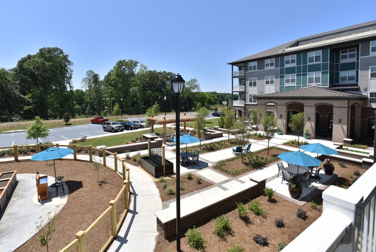 Aerial view of a modern apartment community courtyard with seating areas, blue umbrellas, and landscaped paths.