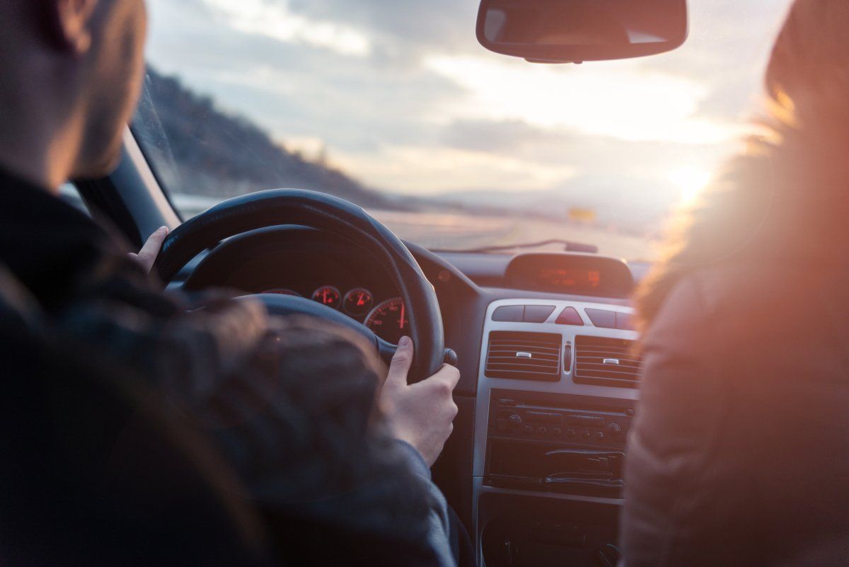Autofahrer sitzt am Steuer im Auto mit Sonnenuntergang