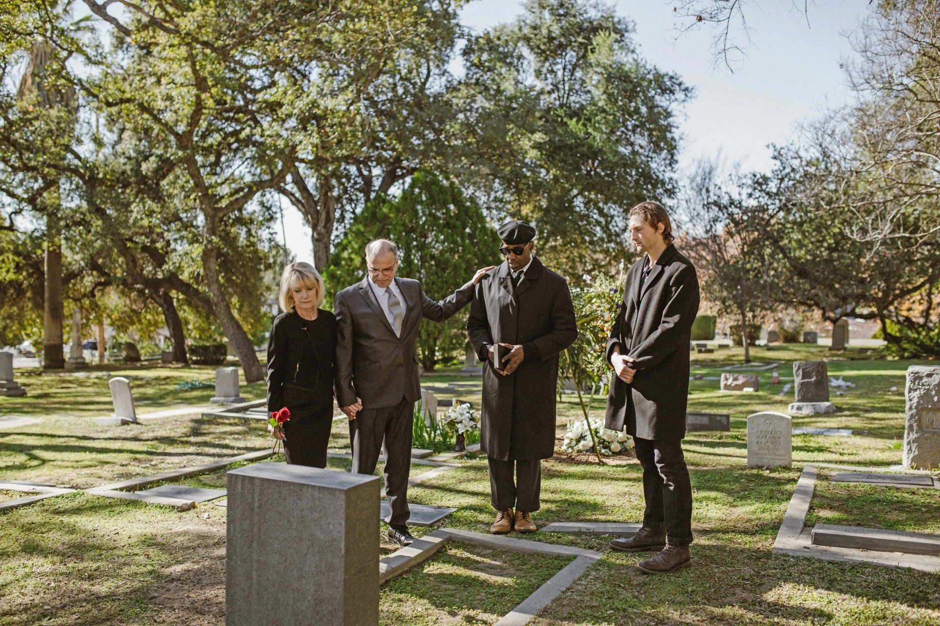 Begräbnis mit vier Personen vor dem Grabstein auf der Wiese