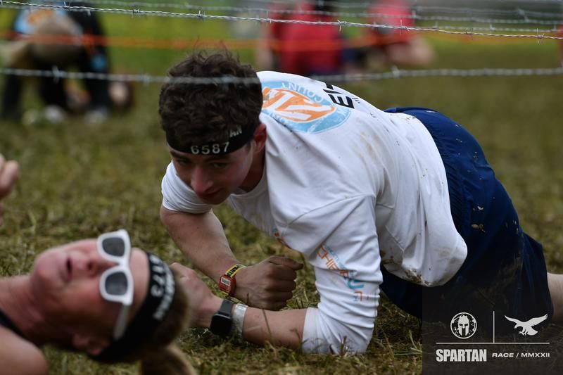 A man and a woman are crawling through a barbed wire fence.