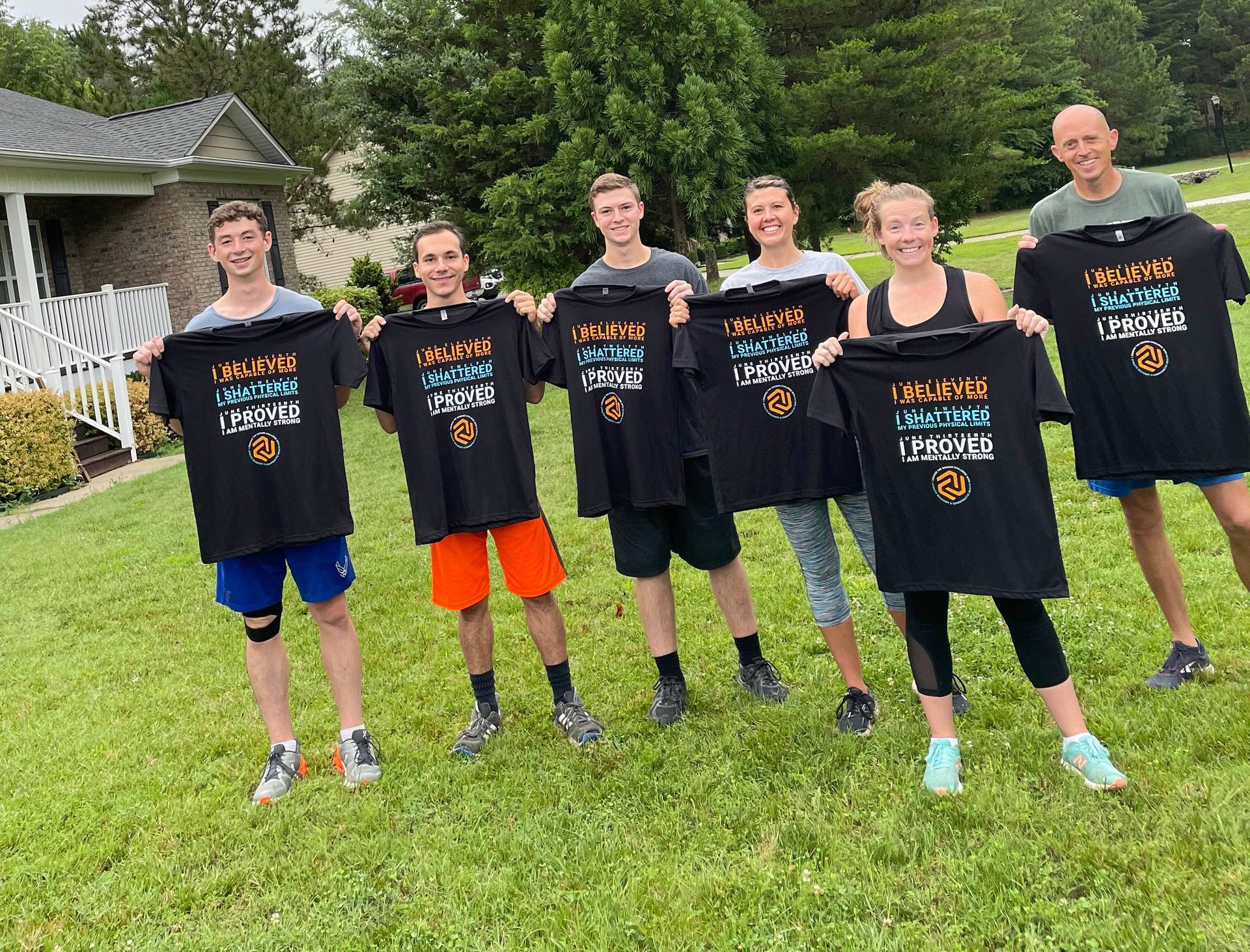 A group of people are standing in a grassy field holding t-shirts.