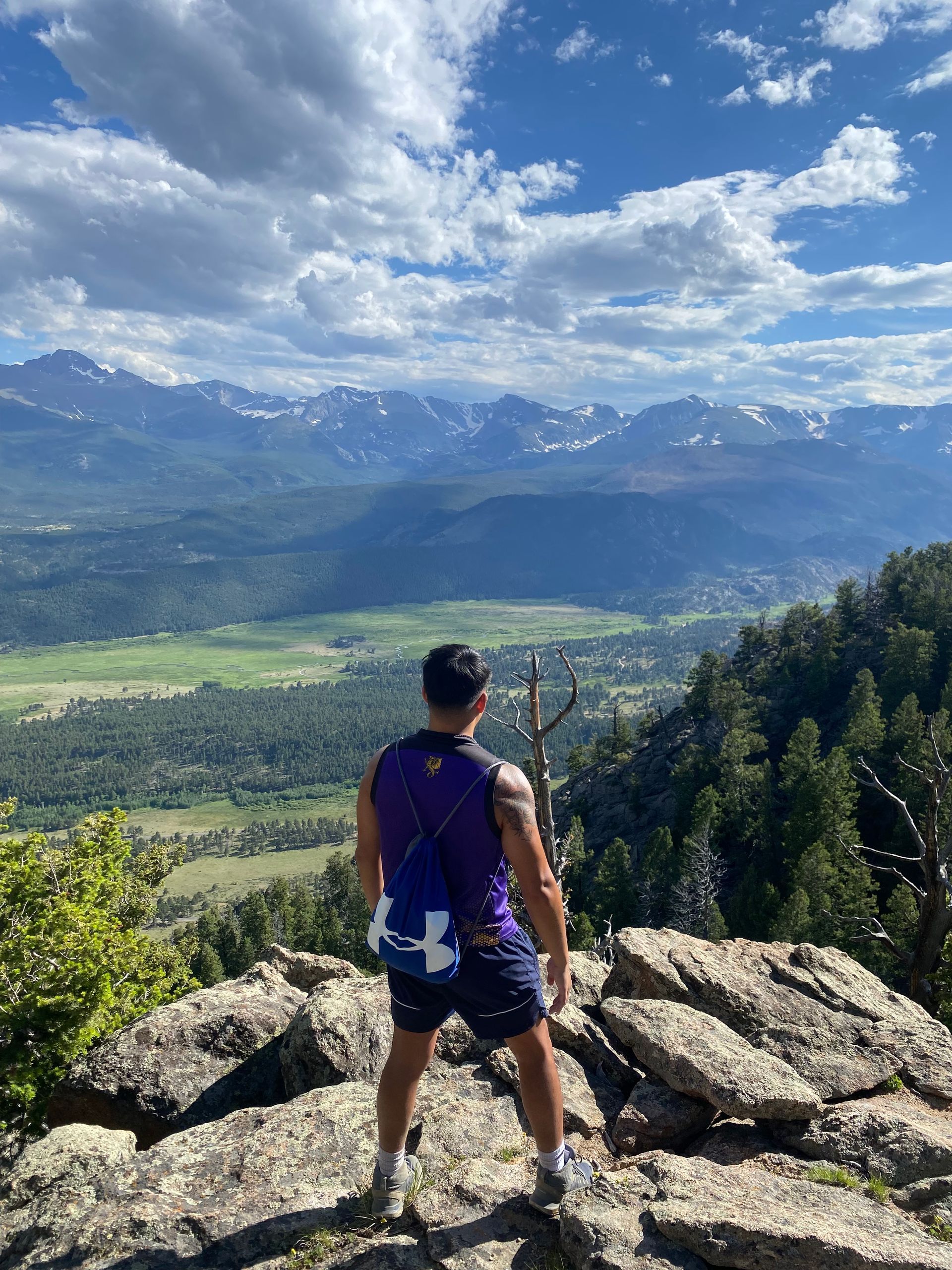 A man is standing on top of a mountain looking out over a valley.