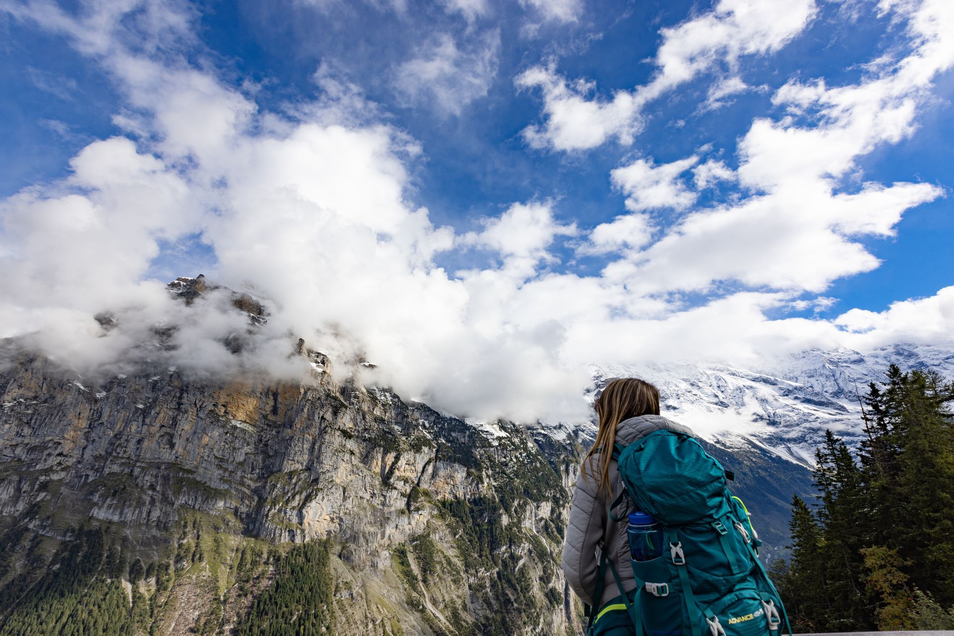 A woman with a backpack is looking at a mountain range.