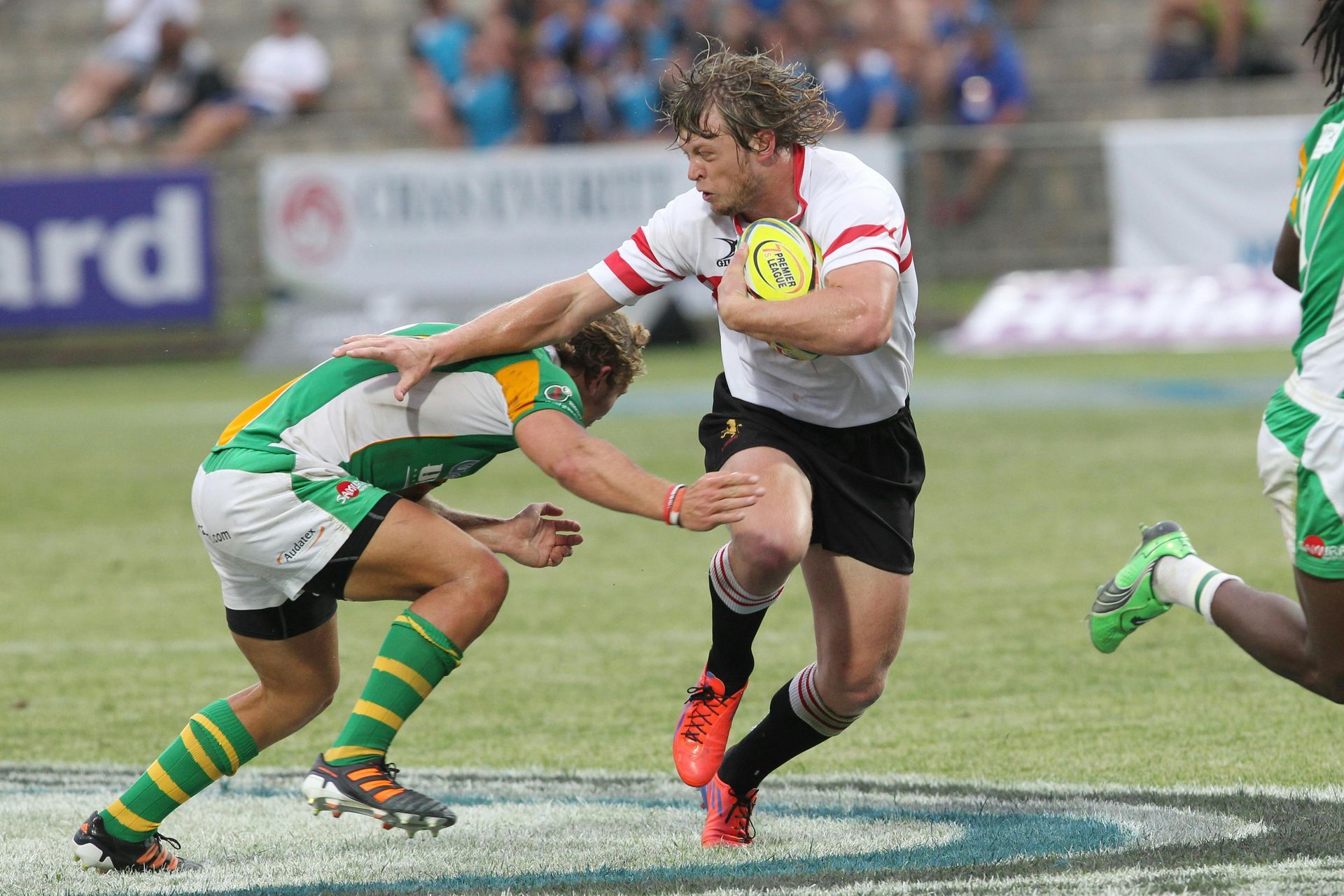 A rugby player runs with the ball while another player tries to tackle him