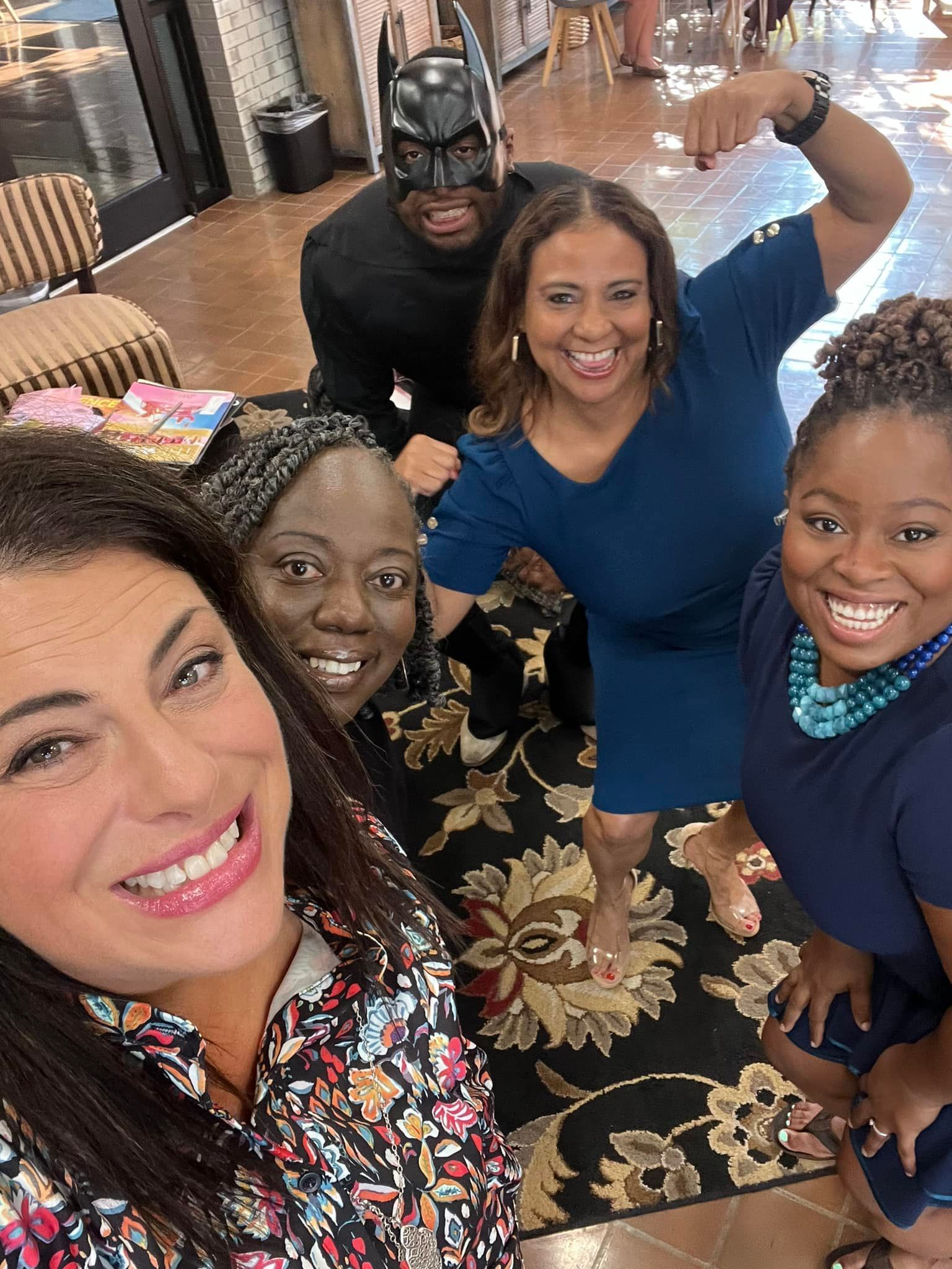 Five people smiling for a selfie in a living room, with a Batman figure in the background.