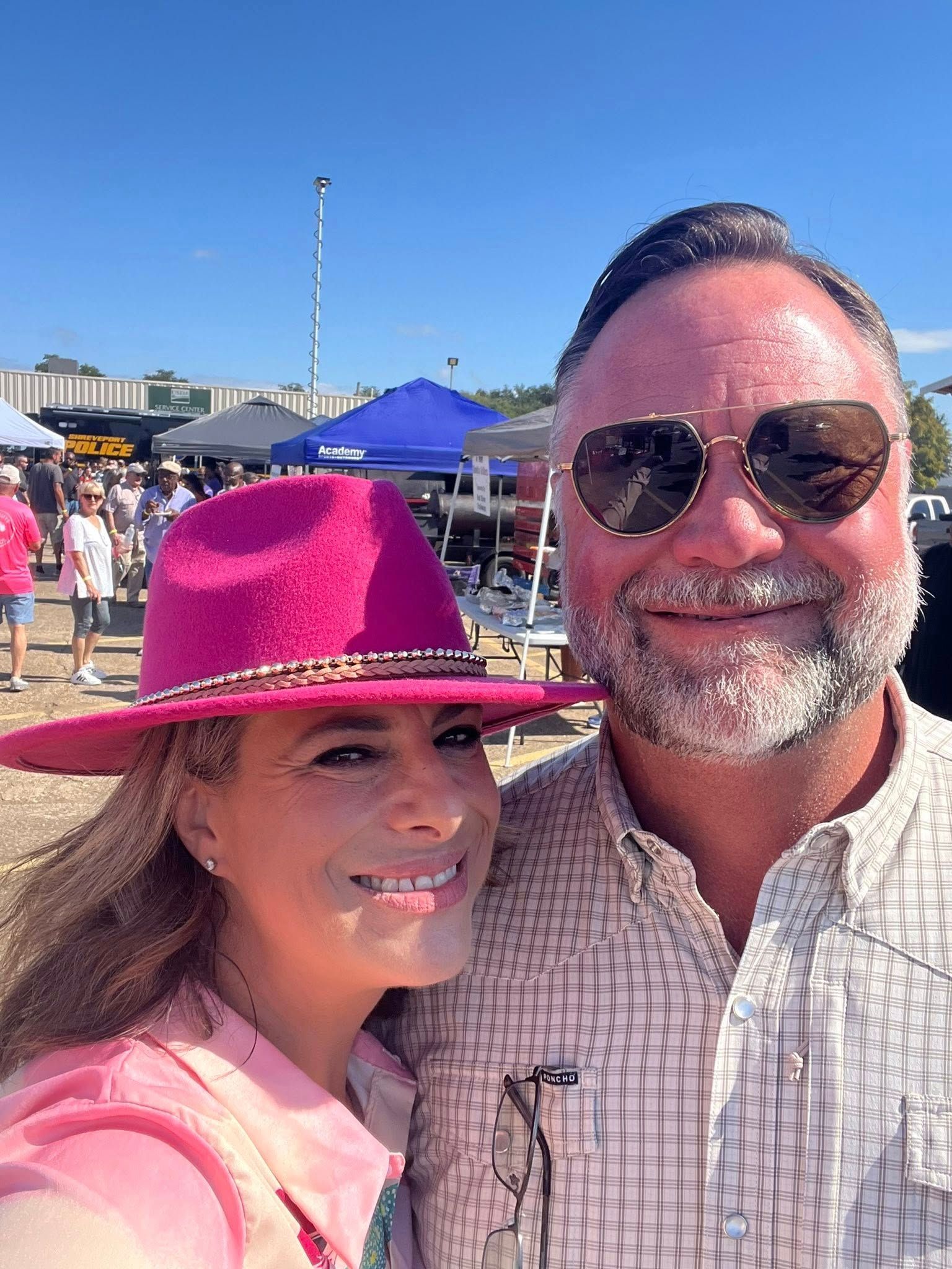 Smiling couple in pink hats taking a selfie outdoors at a sunny beach event