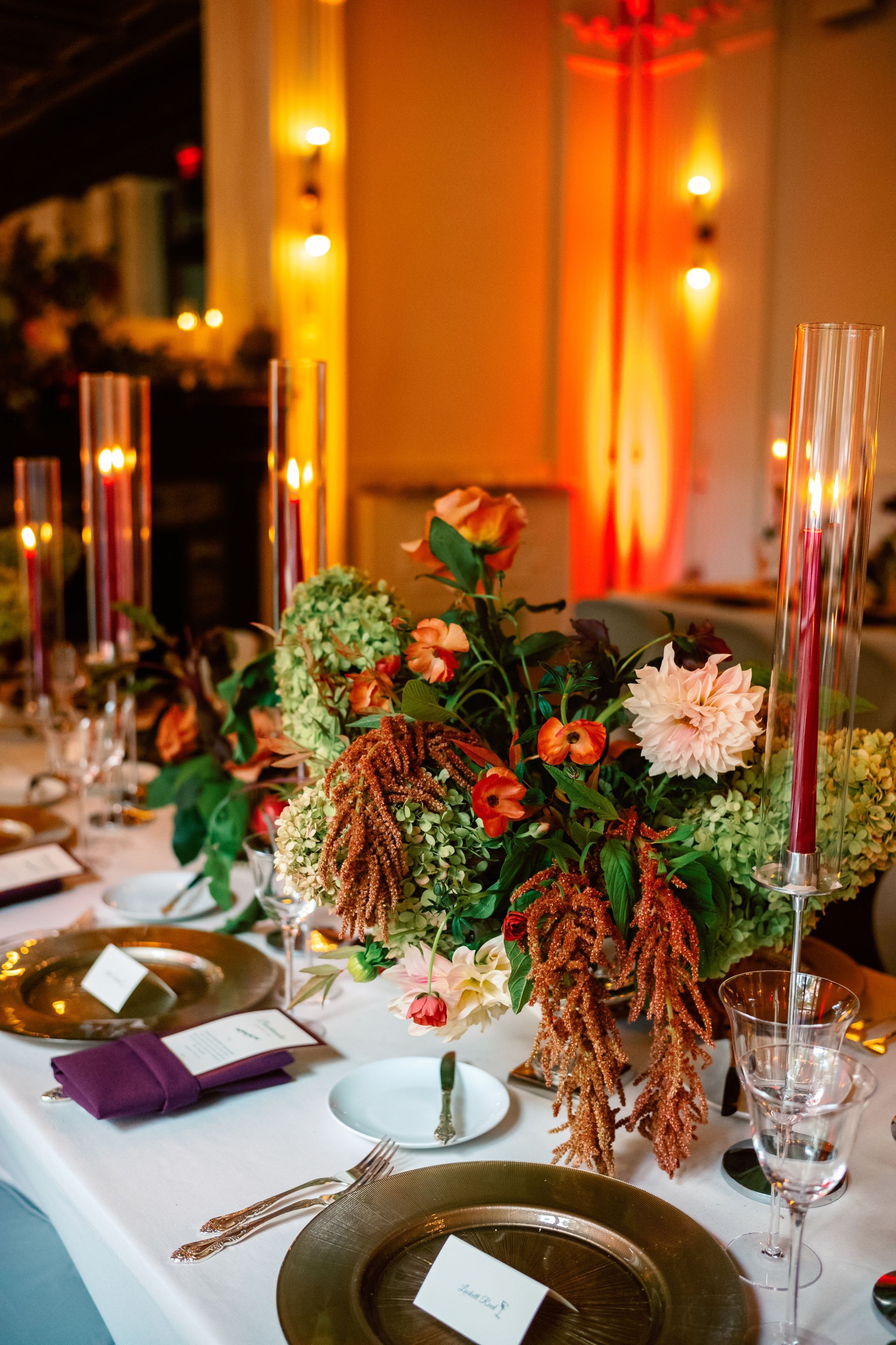 Elegant table setting with floral centerpiece, gold chargers, and burgundy accents; warm lighting.