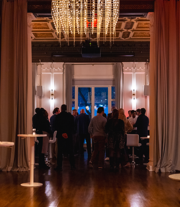 A group of people are gathered in a room with a chandelier hanging from the ceiling