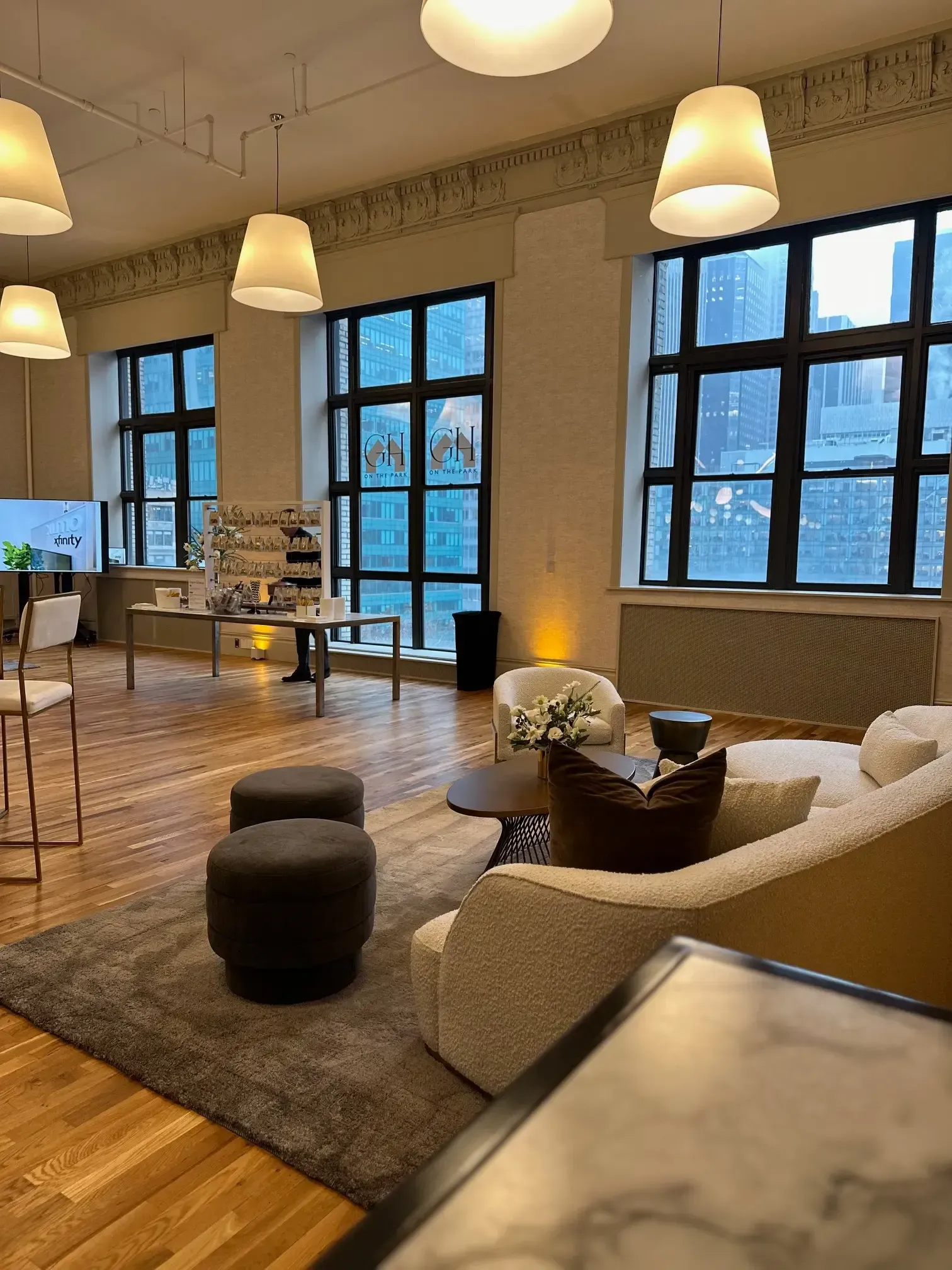 Spacious room with large windows, modern furniture, and cityscape view. Soft lighting, hardwood floors, and a neutral color palette.