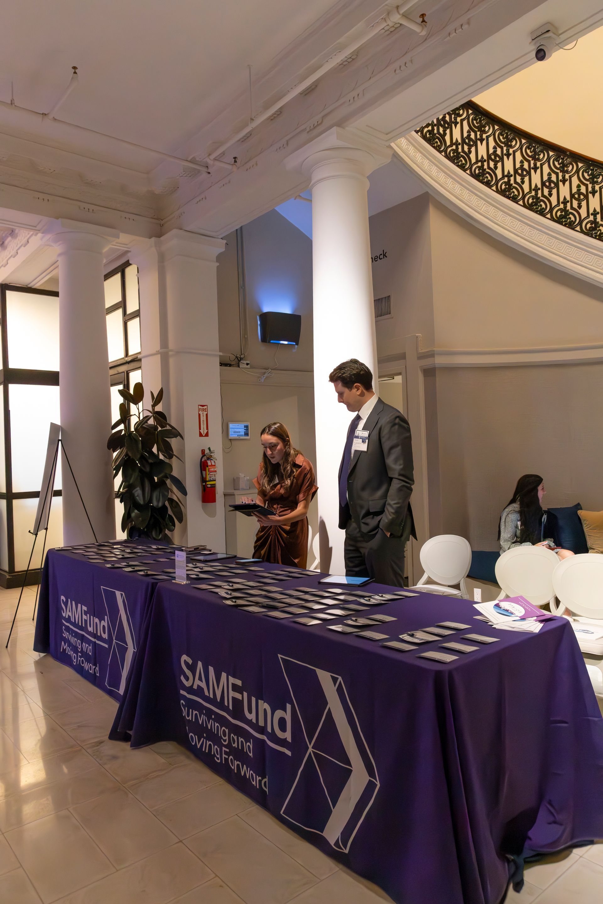 People at registration table with "SAMFund" sign. Interior, formal setting, purple table cloth.