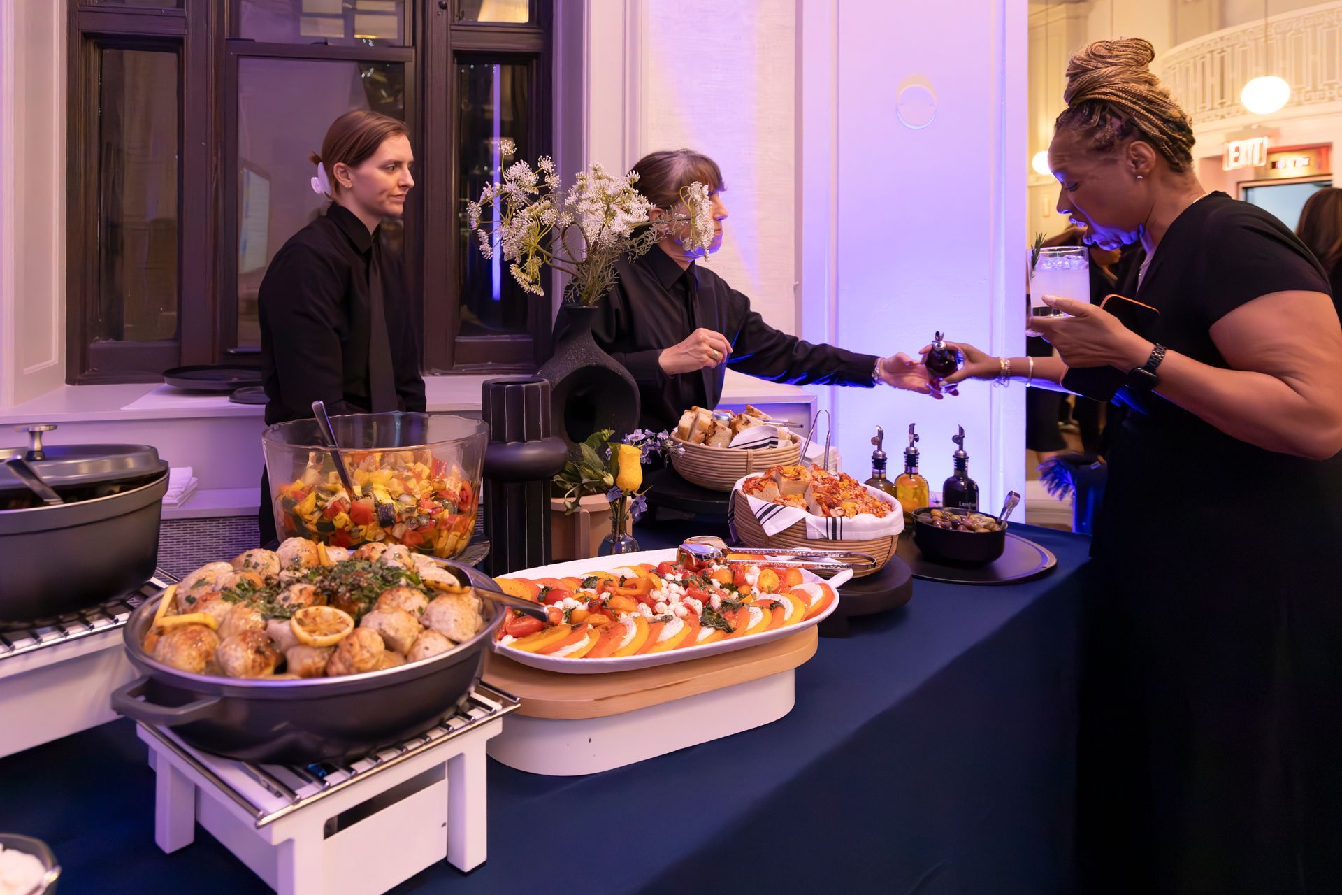 Food server handing a drink to a guest at an outdoor event with a buffet table.
