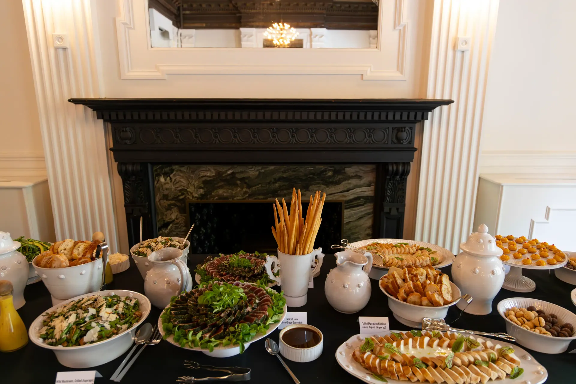 Table setting with gold chargers, floral arrangements, food, and someone taking a photo with a phone.
