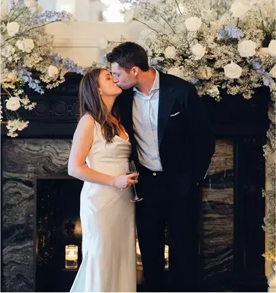 A bride and groom kissing in front of a fireplace