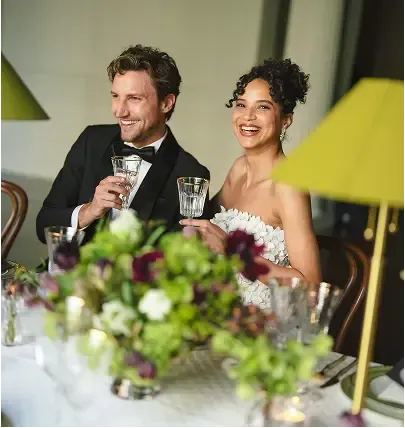 A bride and groom are sitting at a table with glasses of wine