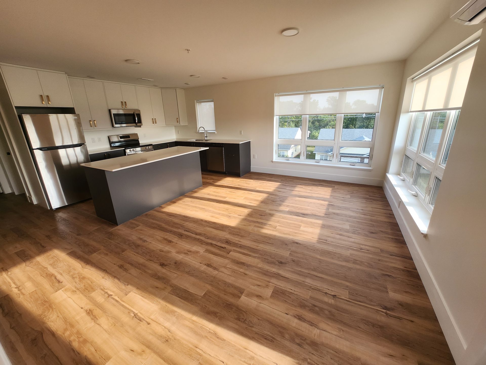 Kitchen with large island, stainless steel appliances, hardwood floor, and 2 large windows. At The Simmons apartment building in Summerside, PEI.