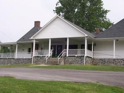 A white building with a stone foundation, a covered porch, and a central staircase under a gable roof.