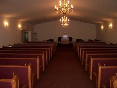 An interior view of a church sanctuary with rows of pews facing a central podium under two hanging chandeliers.