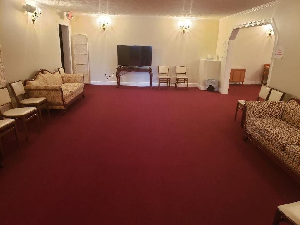 A room with red carpeting, furnished with sofas and chairs arranged for seating, facing a television on a stand.