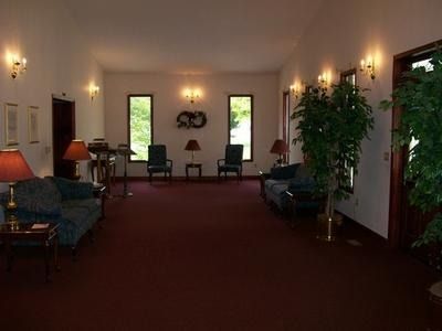 A quiet, dimly lit waiting room with burgundy carpeting, dark blue sofas, two chairs by windows, and warm wall lighting.