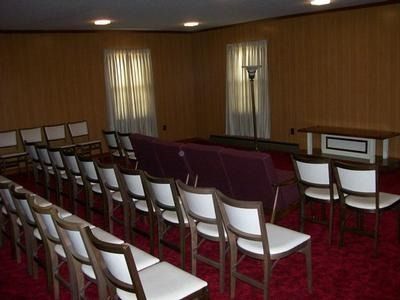 A room with rows of chairs facing a long purple bench and a small wooden podium, set against wood-paneled walls.