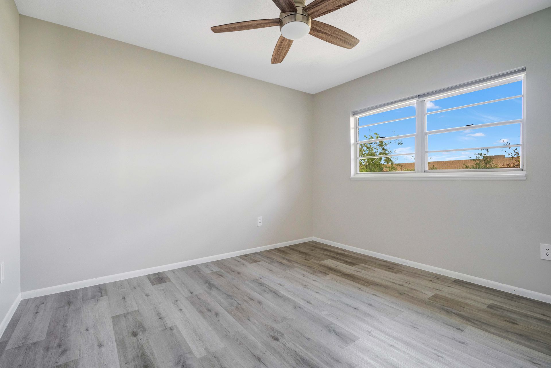 An empty bedroom with a ceiling fan and a window.