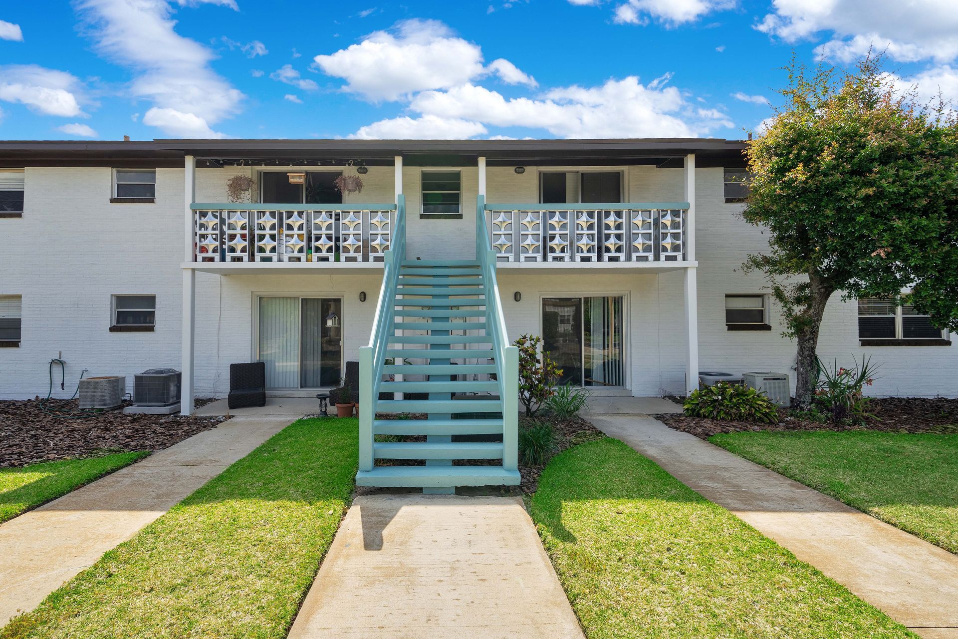 A white apartment building with blue stairs leading up to the second floor.