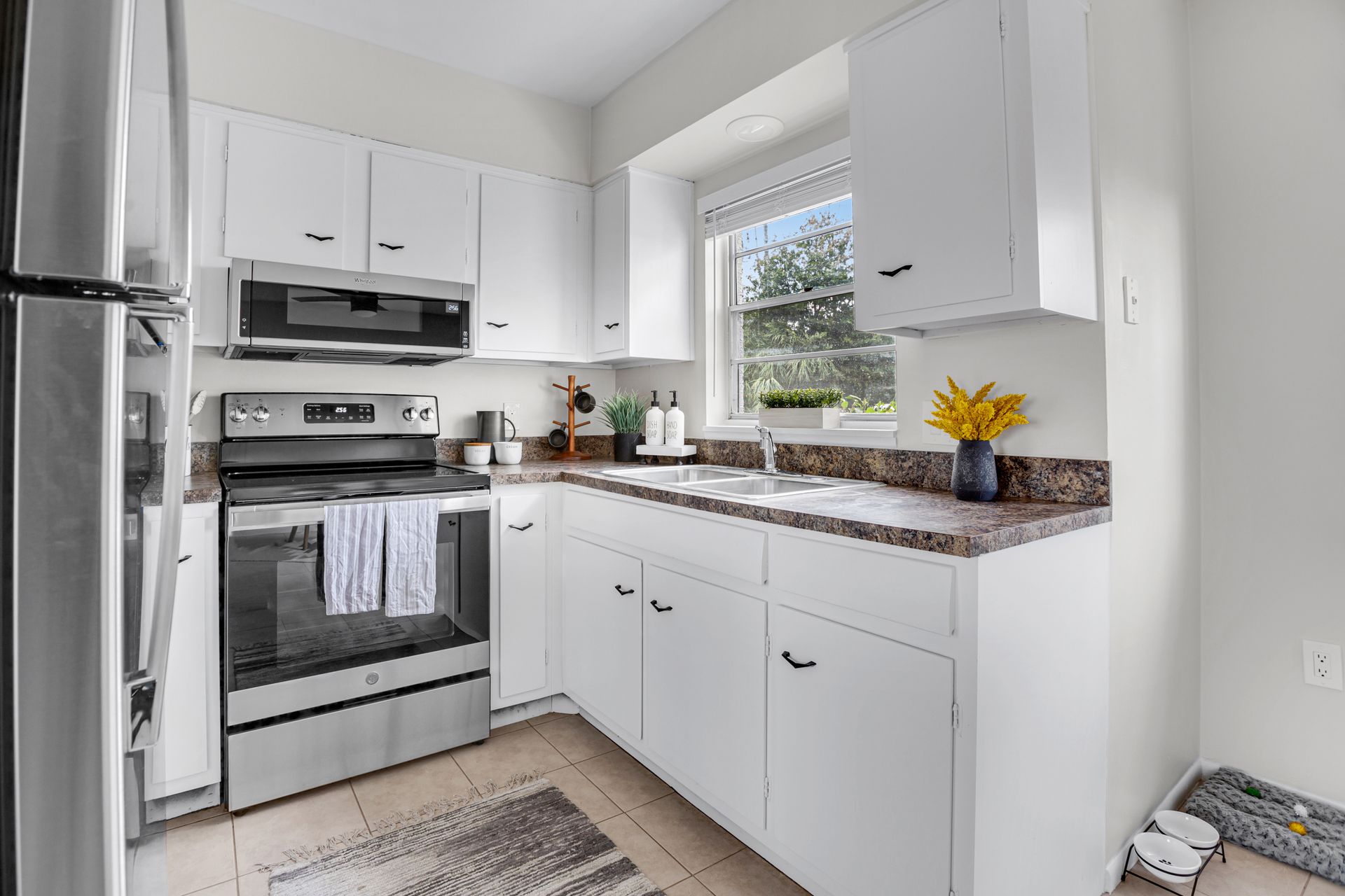 A kitchen with white cabinets , stainless steel appliances , a refrigerator and a window.