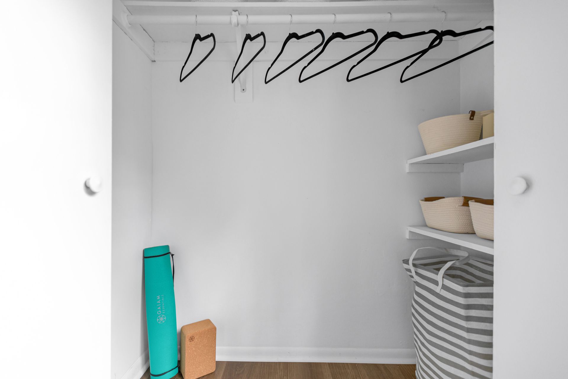 A closet with a yoga mat , baskets , and clothes hangers.