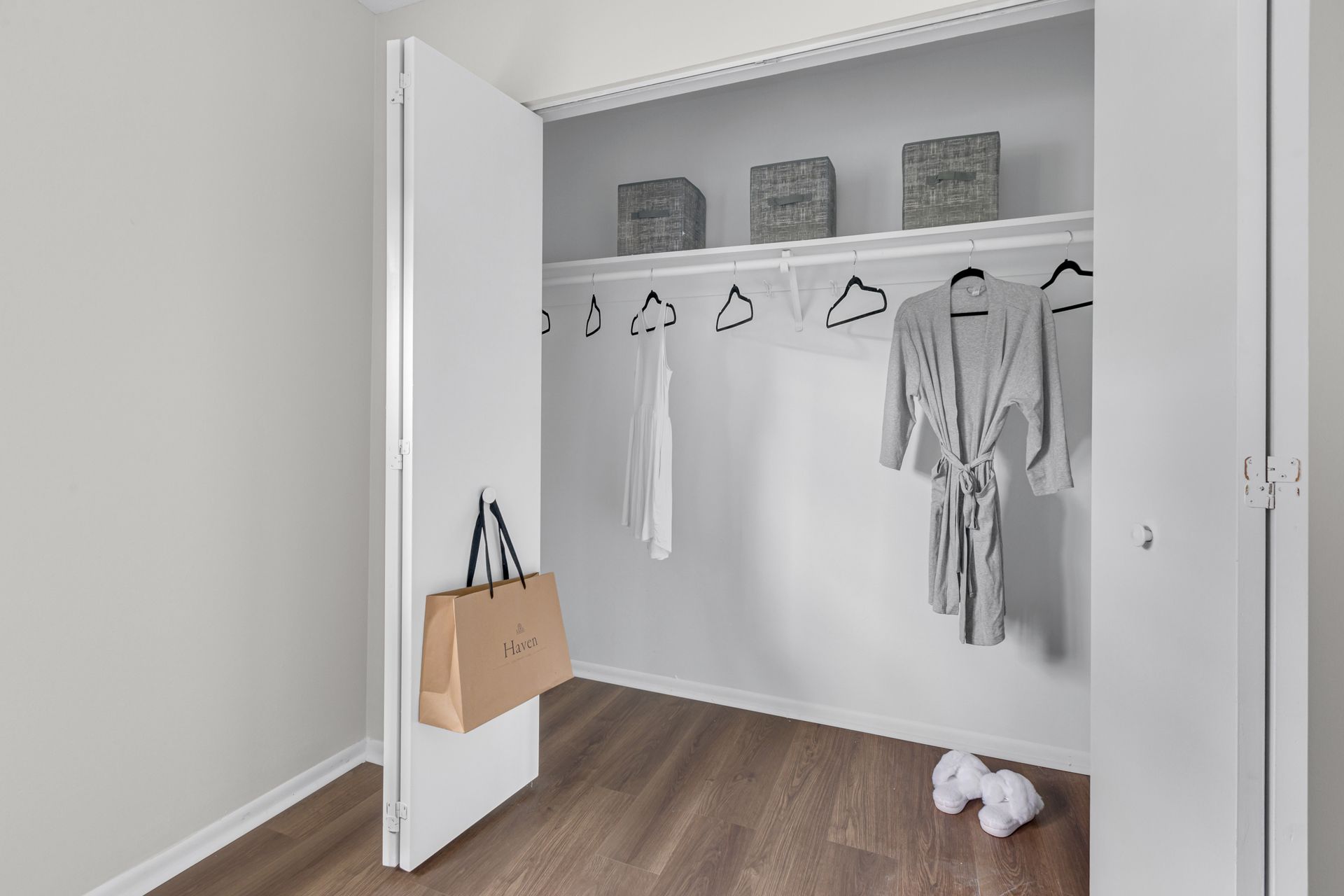 A walk in closet with clothes hanging on racks and a bag hanging on the door.
