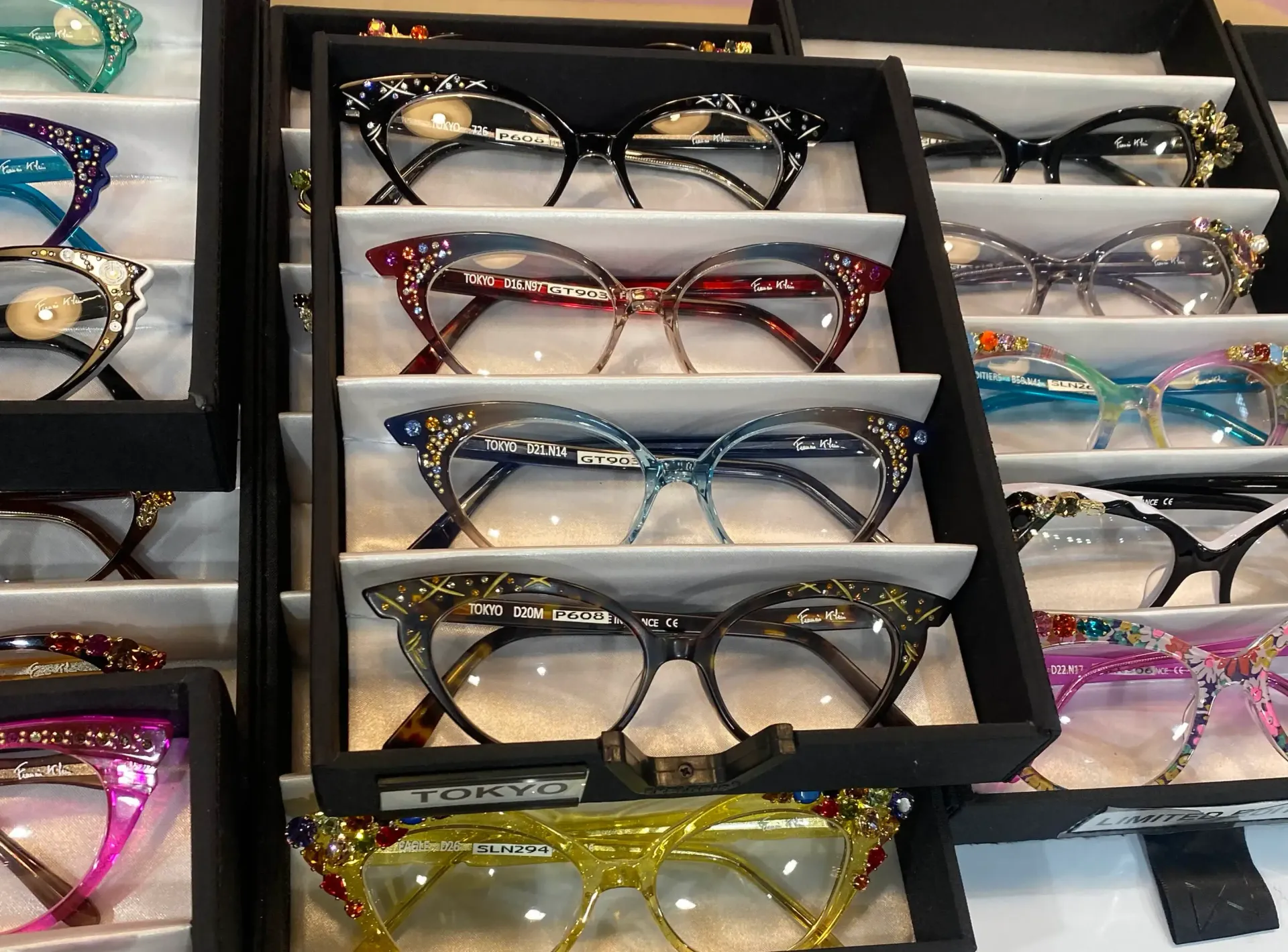 Display of eyeglasses in various colors and patterns, arranged in tiered display cases.