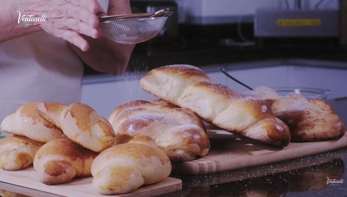 Uma pessoa está polvilhando açúcar de confeiteiro em um monte de pão em uma tábua de corte.