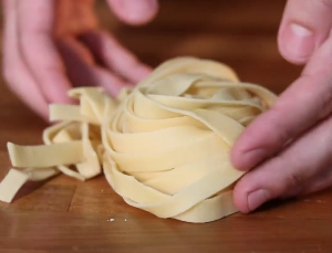 Uma pessoa está segurando um pedaço de macarrão em uma mesa de madeira.