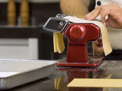 Uma pessoa está usando uma máquina de macarrão vermelha para fazer macarrão