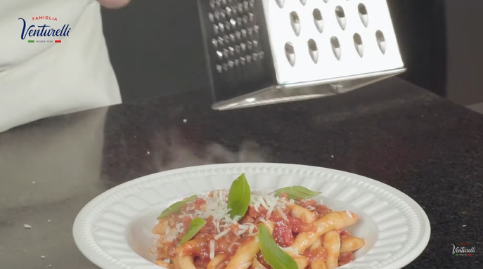 Uma pessoa está ralando queijo em um prato de macarrão.