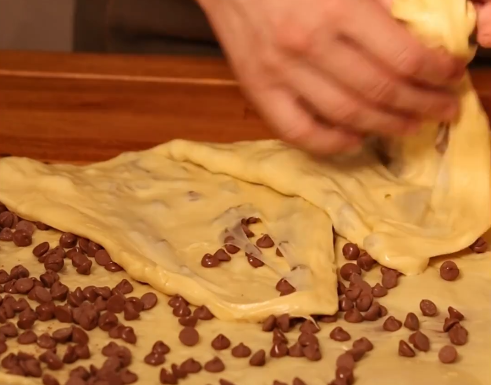 Uma pessoa está espalhando gotas de chocolate em um pedaço de massa