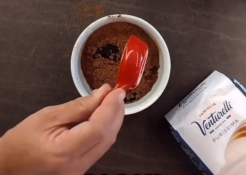 Uma pessoa está segurando uma espátula sobre uma tigela de chocolate