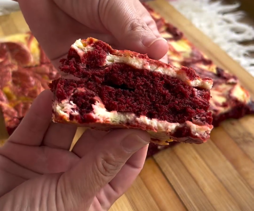 Uma pessoa está segurando um pedaço de bolo red velvet com uma mordida.