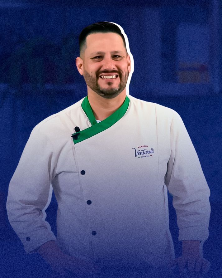 Um homem com barba está vestindo uma jaqueta de chef branca com gola verde.